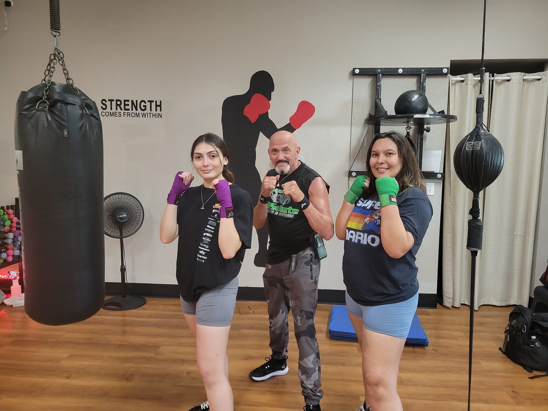 A man and two women are posing for a picture in a boxing gym.