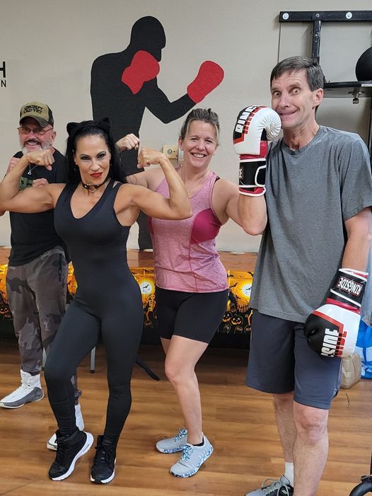 A group of people wearing boxing gloves are posing for a picture in a gym.