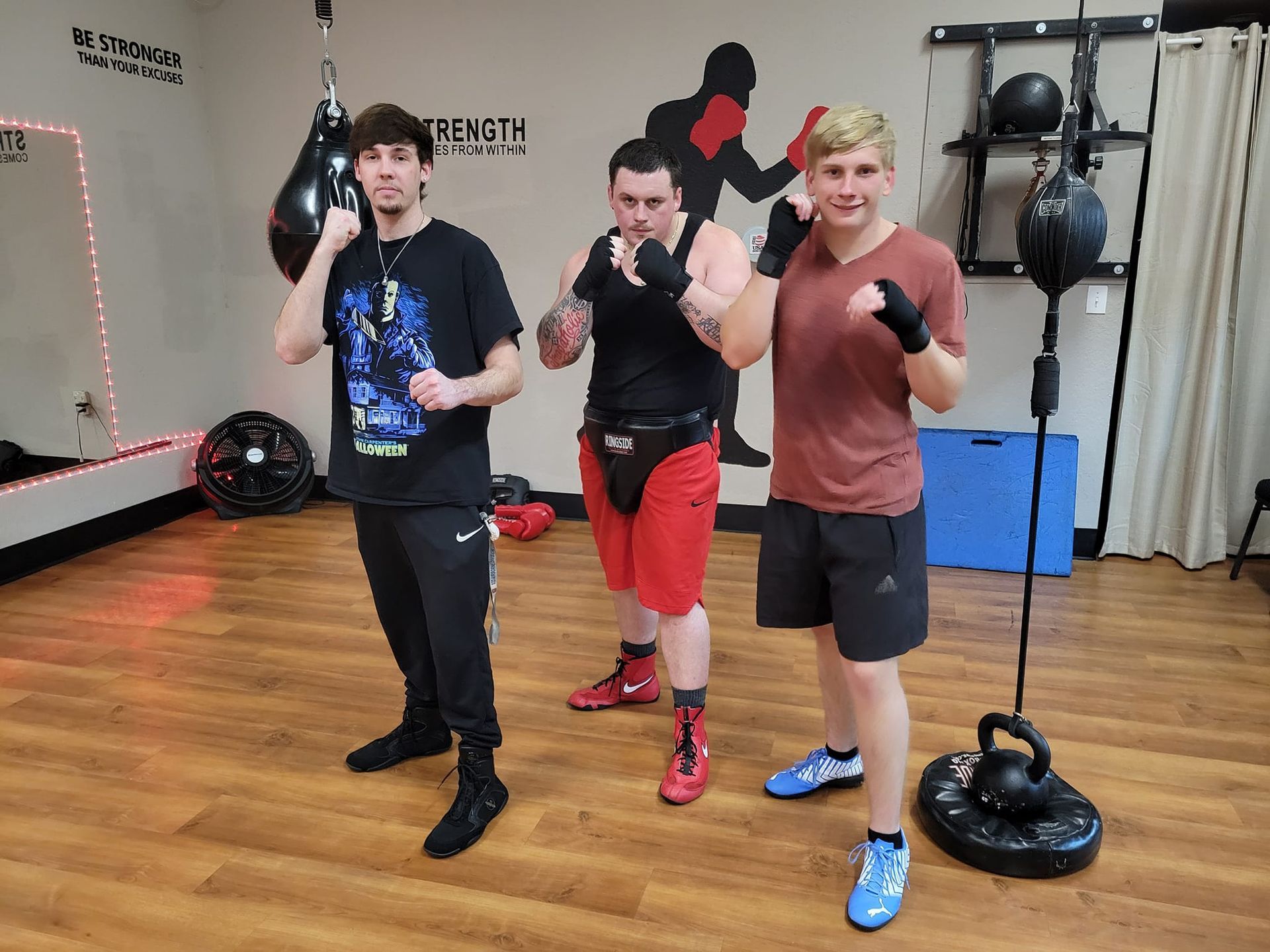 Three young men are standing next to each other in a boxing gym.