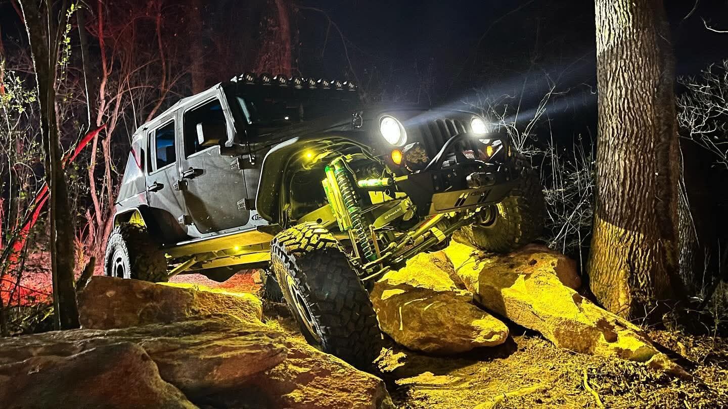 An aerial view of a jeep driving down a dirt road in the woods.