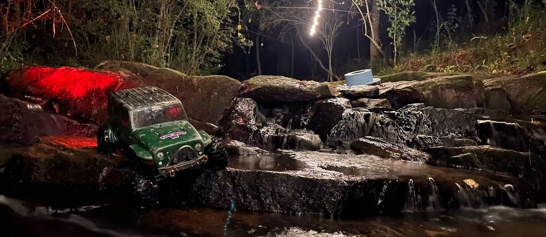 A waterfall is surrounded by rocks and trees at night.