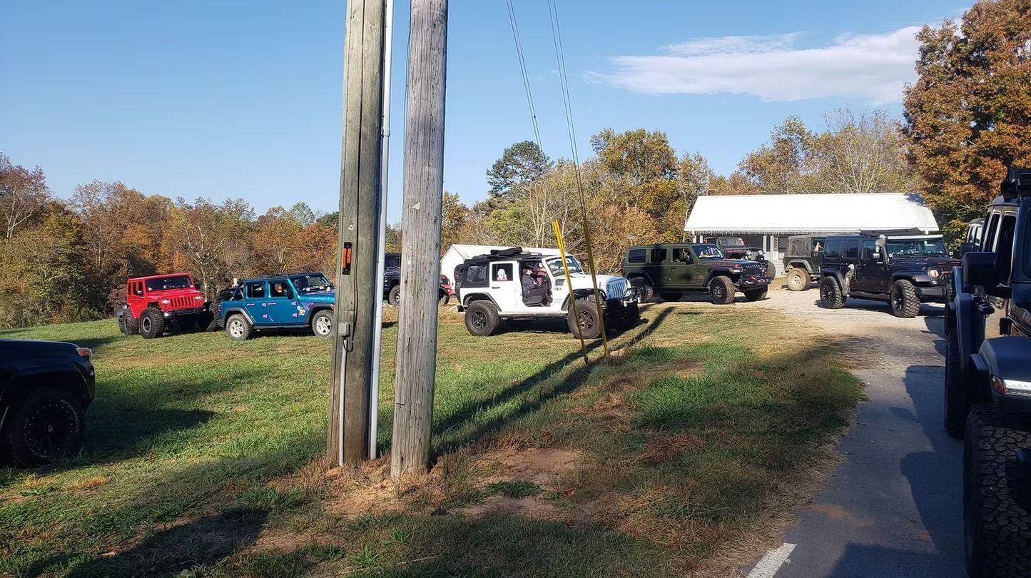 A group of jeep 's are parked on the side of a dirt road.