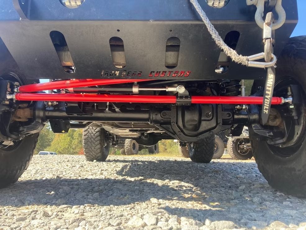 A close up of a jeep 's front suspension on a gravel road