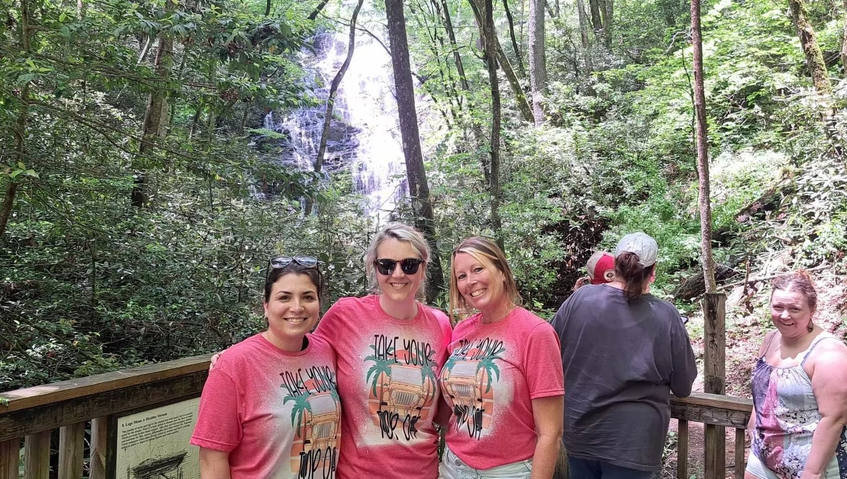 A group of women are posing for a picture in front of a waterfall.