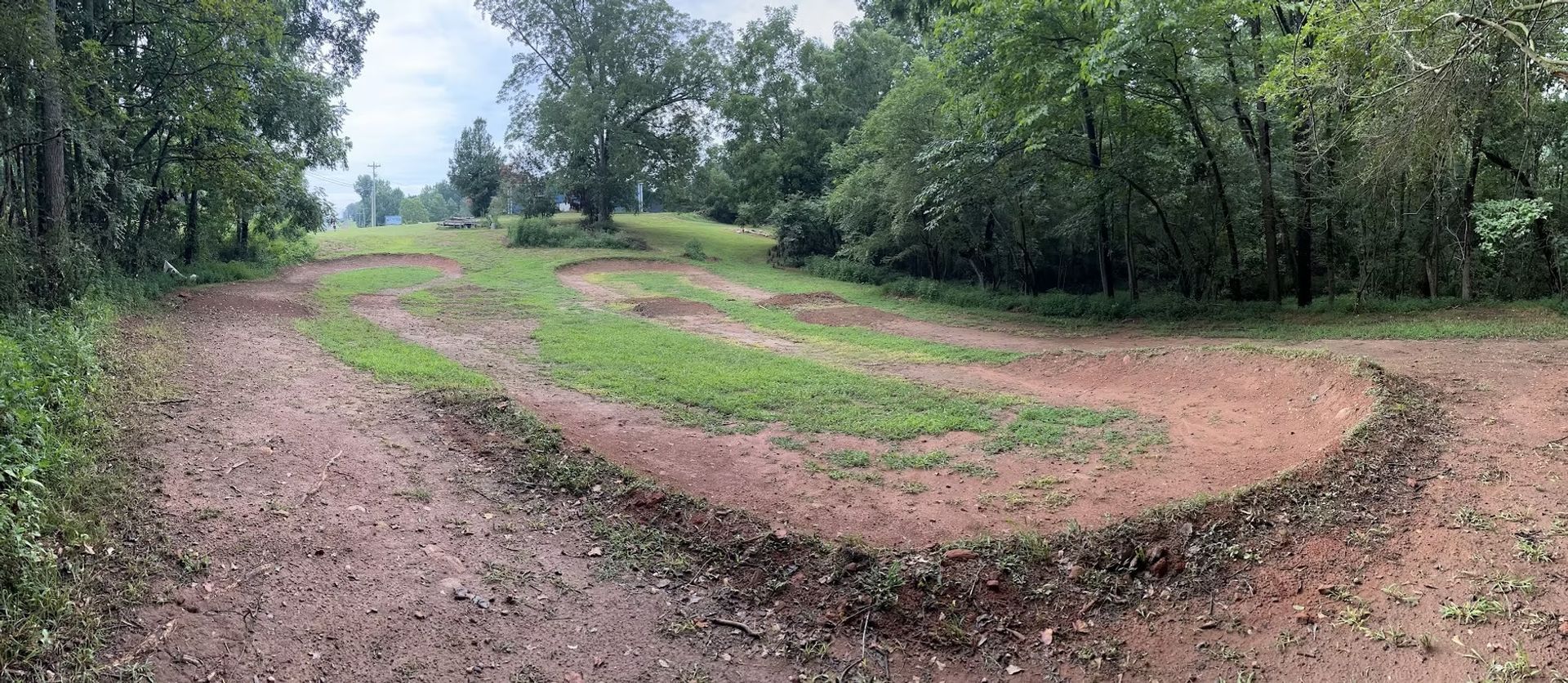 A dirt road going through a grassy field surrounded by trees.
