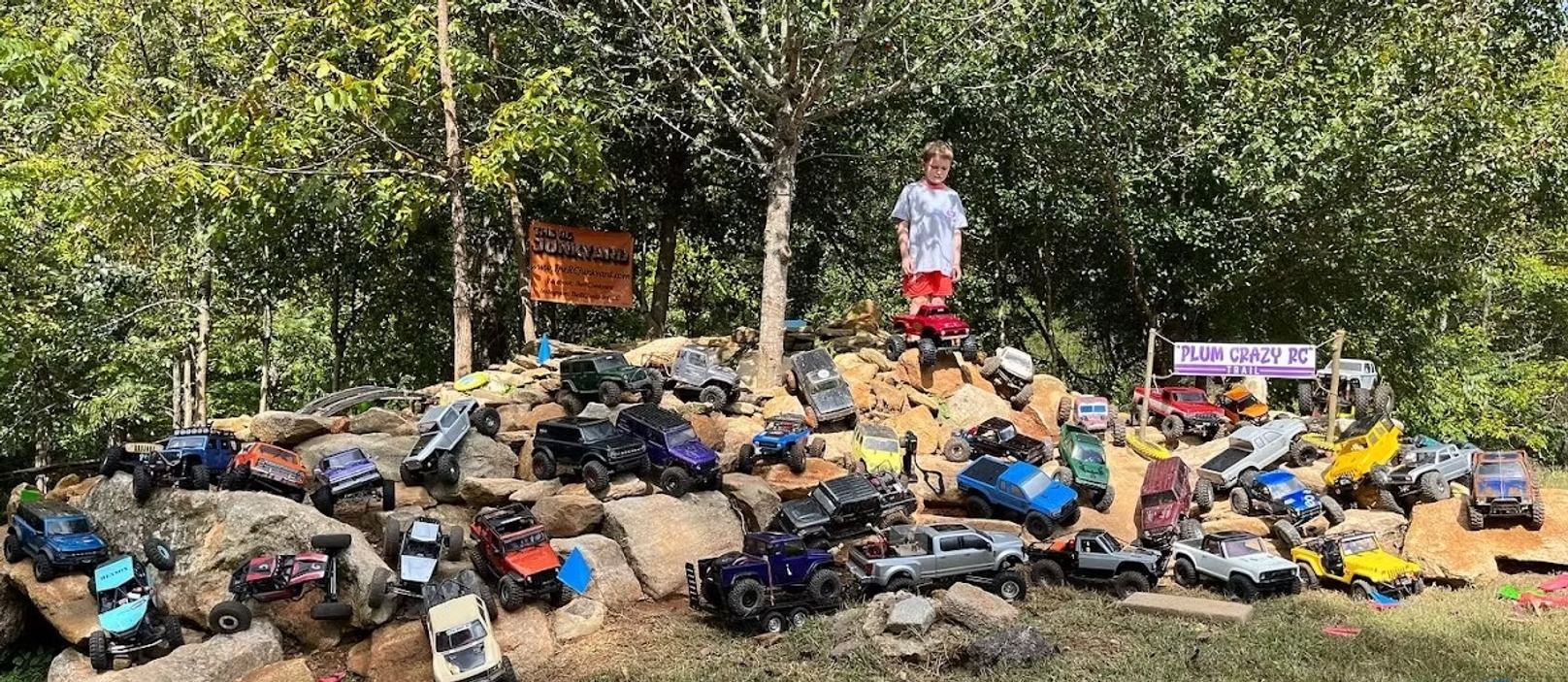 A young boy is standing on top of a pile of toy cars.