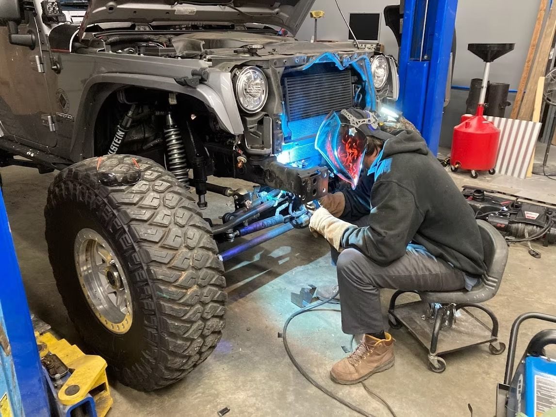 A man is welding a jeep in a garage.