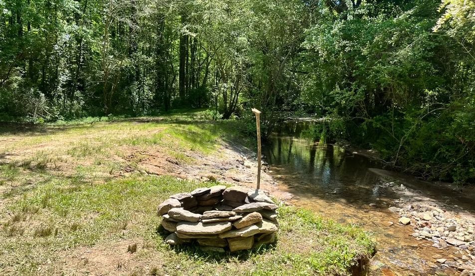 A fire pit is sitting in the middle of a grassy field next to a river.
