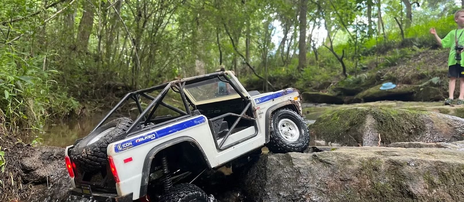 A remote control jeep is driving through the mud in the woods.