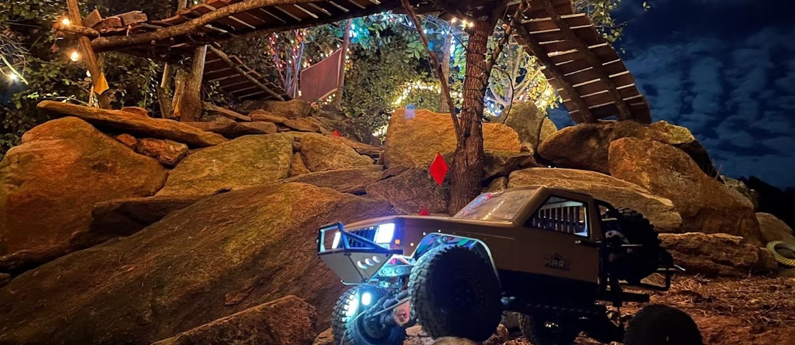 A rc truck is driving down a dirt road at night under a bridge.