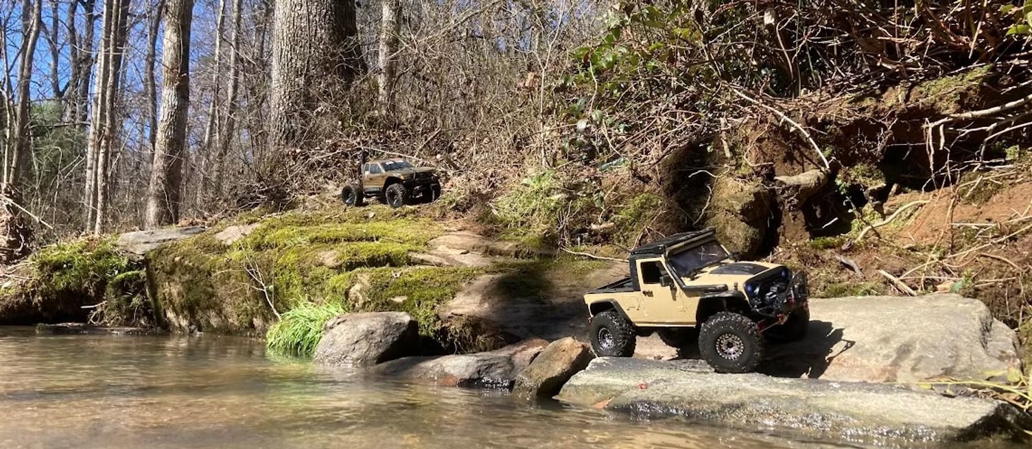 A jeep is driving through a river in the woods.