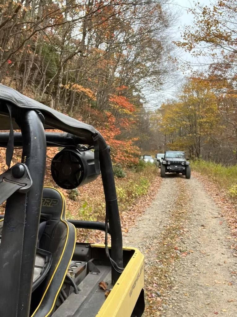A yellow atv is driving down a dirt road in the woods.