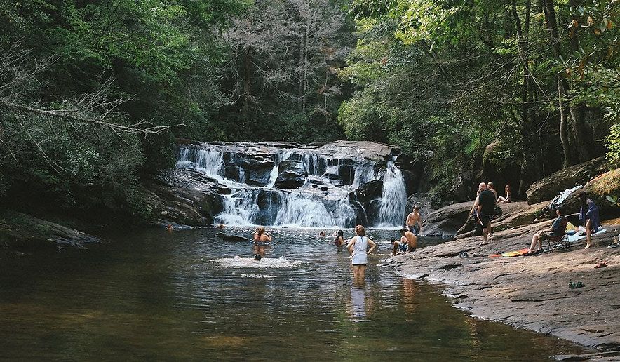 A group of people are swimming in a river near a waterfall.