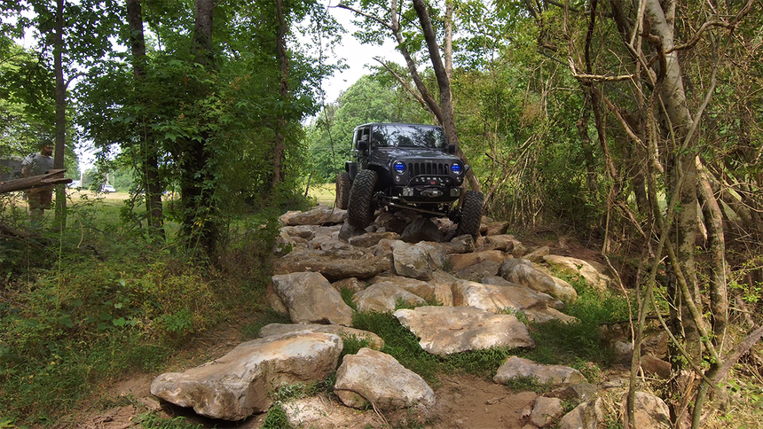 A yellow jeep is parked on the side of a dirt road in the woods.