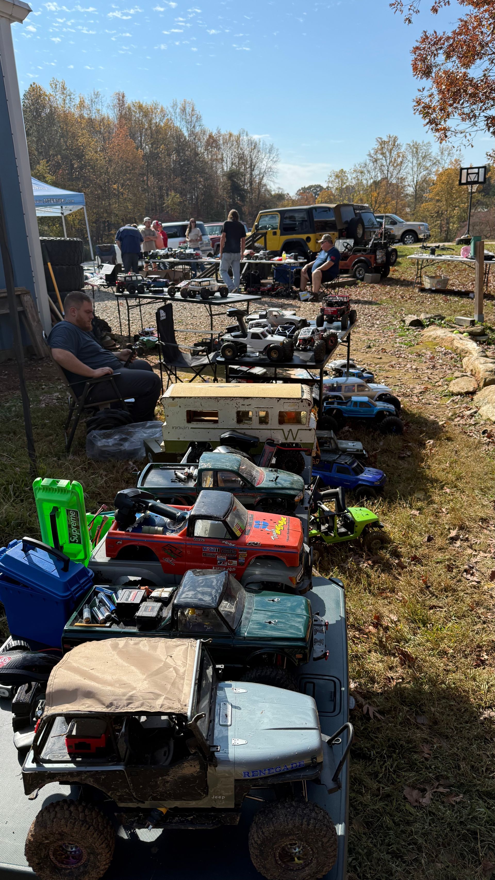 RC cars and parts displayed on tables outdoors, sunny day, people in the background.