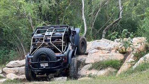 A jeep is driving down a rocky trail in the woods.