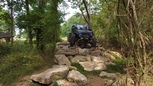A jeep is driving down a rocky trail in the woods.