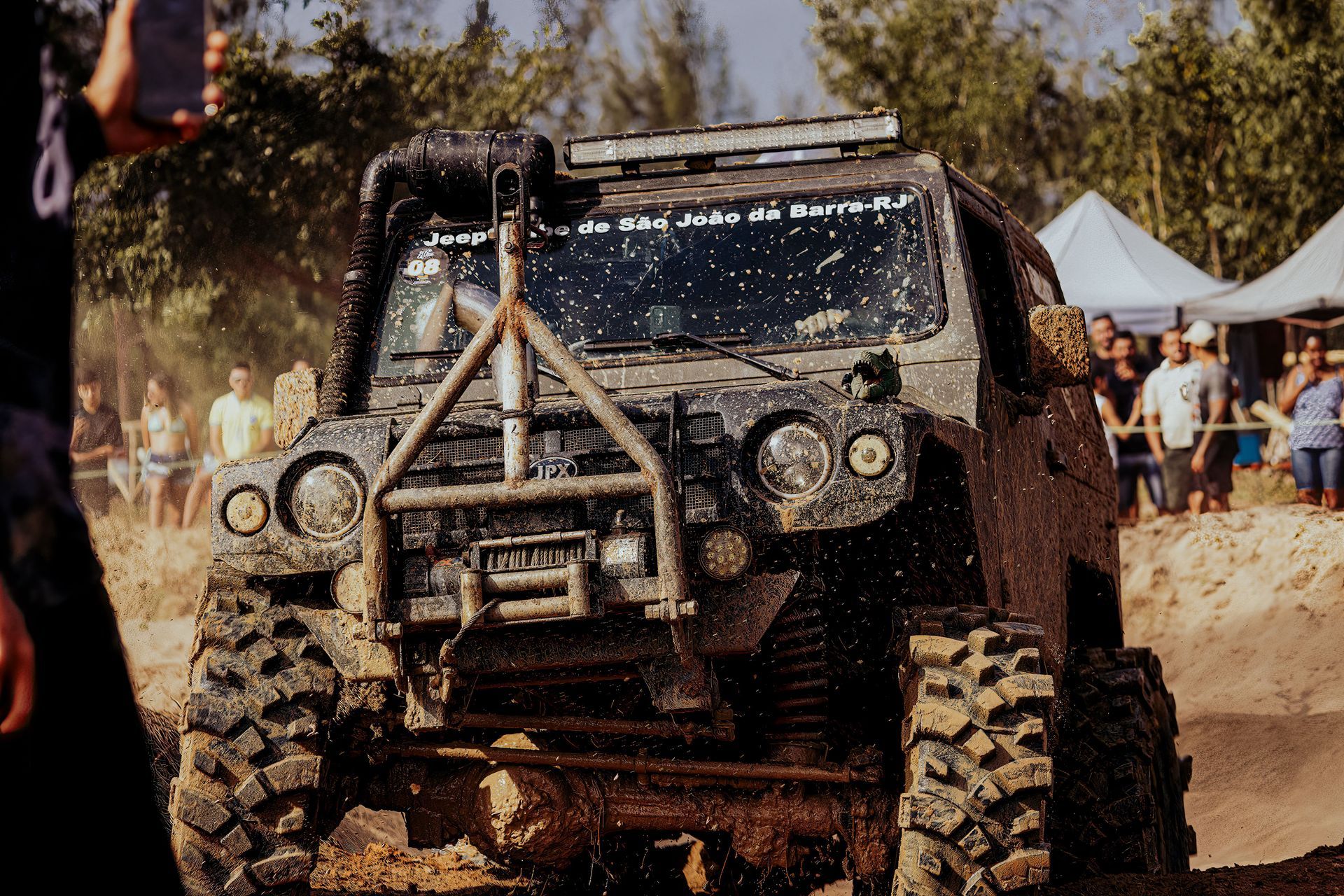 Mud-covered off-road truck with huge tires driving through a muddy outdoor obstacle course