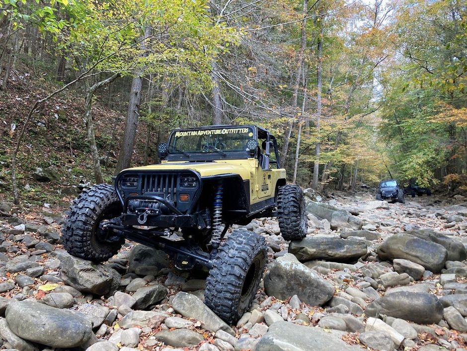A black jeep is driving down a rocky path in the woods.
