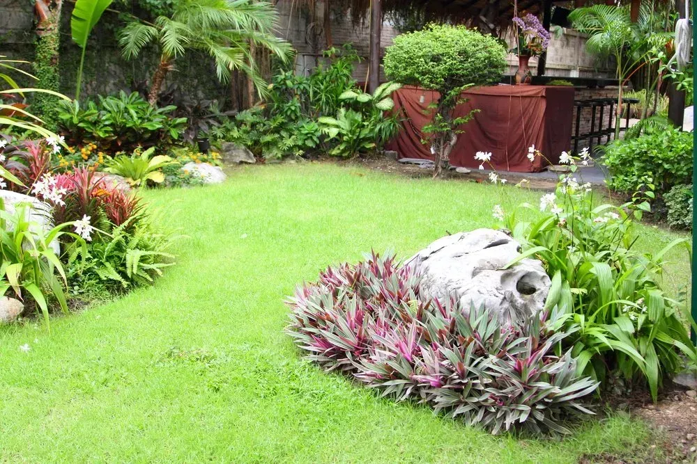 Lush Green Lawn With Colorful Plants and a Large Rock in a Garden Setting — Garden City Slashing in Highfields, QLD