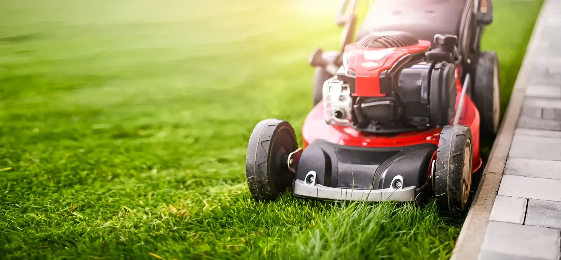 Red Lawnmower Mowing Green Grass Next to a Gray Stone — Garden City Slashing in Toowoomba, QLD