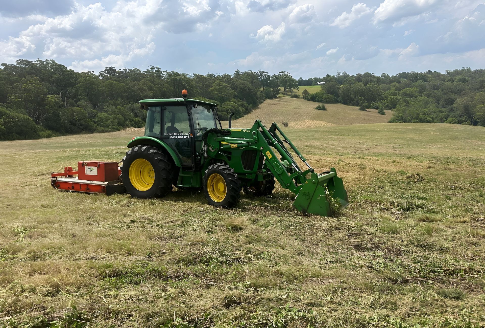 Orange Tractor With Front Loader on a Grassy Field Under a Cloudy Sky — Garden City Slashing in Highfields, QLD