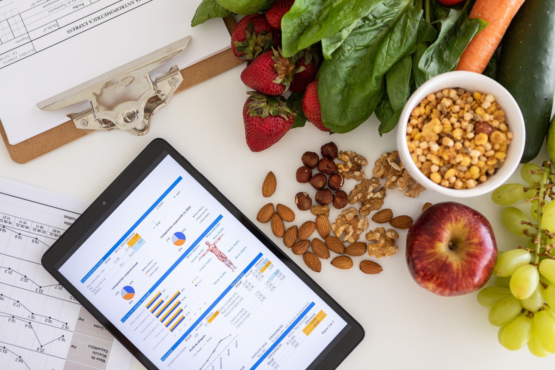 Tablet displaying nutrition data, surrounded by fruits, vegetables, nuts, and grains.