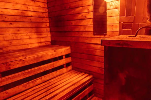 Interior of a wooden sauna, lit with warm red light. Bench and heater visible.