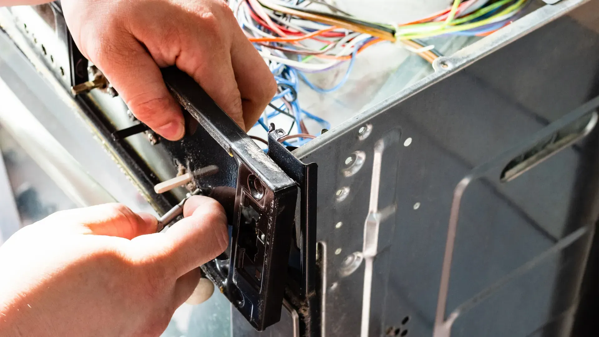 A person is fixing a dishwasher with a screwdriver.