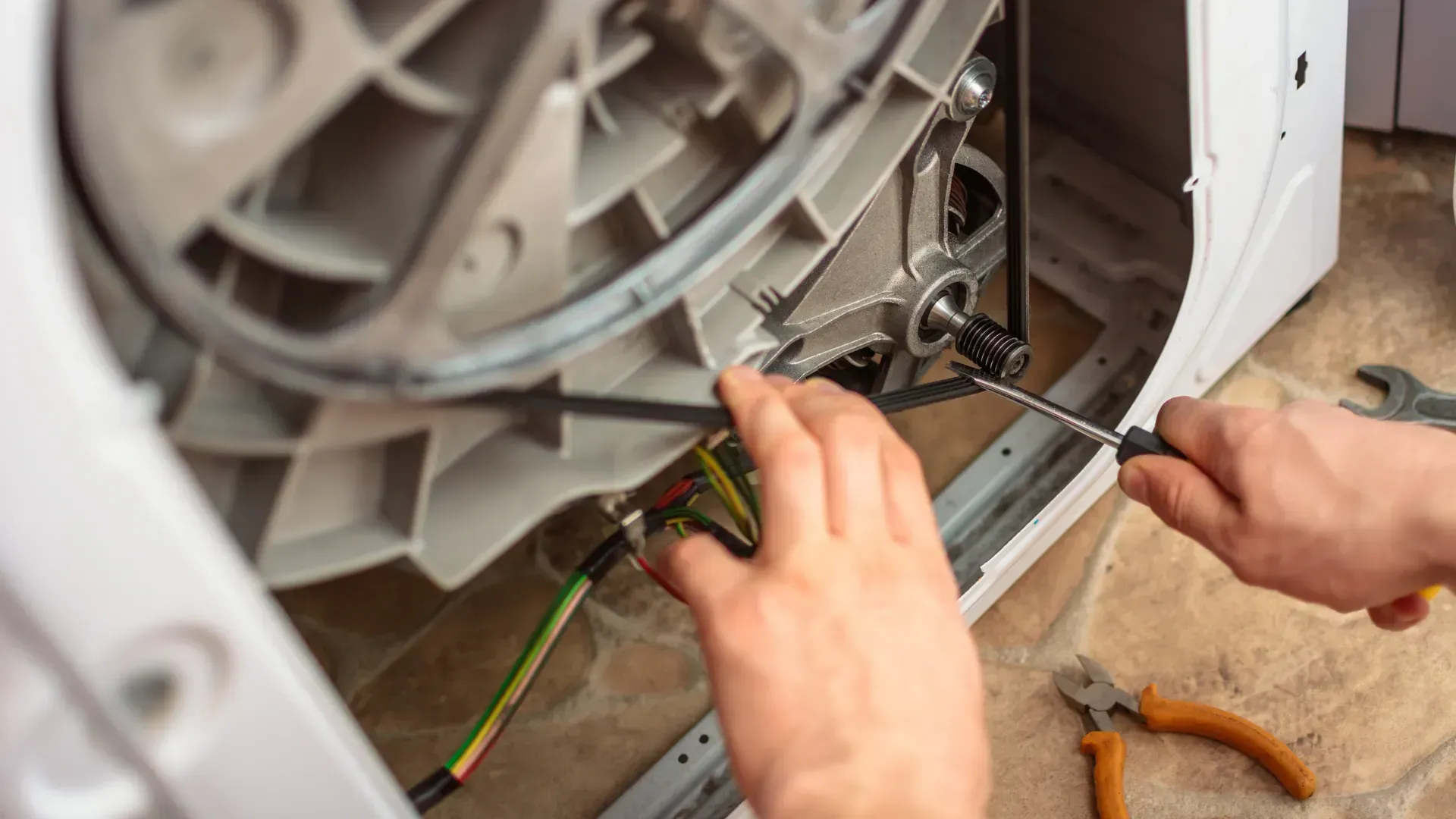 A person is fixing a washing machine with a screwdriver.