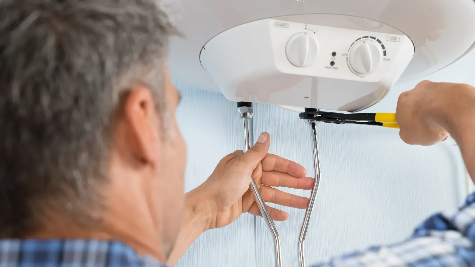 A man is fixing a water heater with a wrench.
