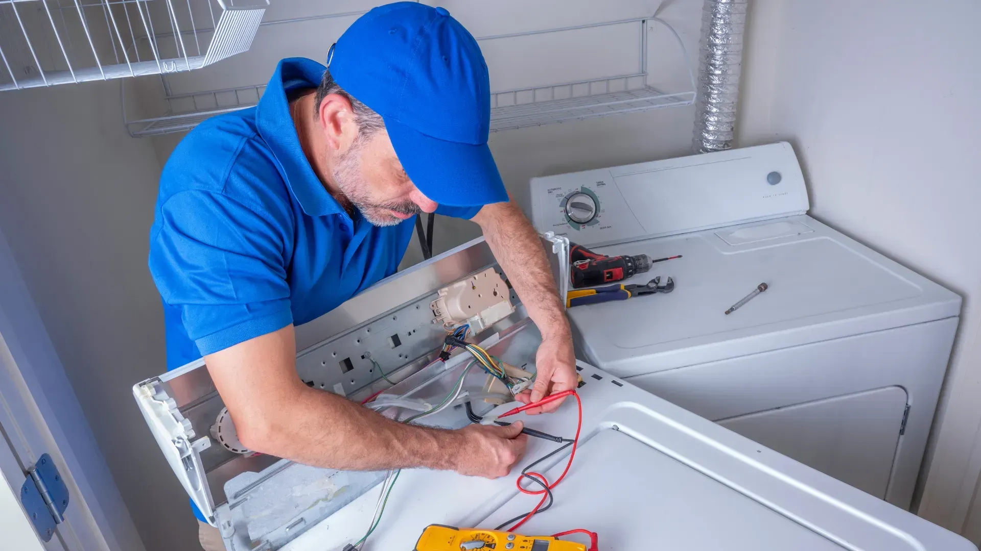 A man is fixing a washer and dryer in a laundry room.