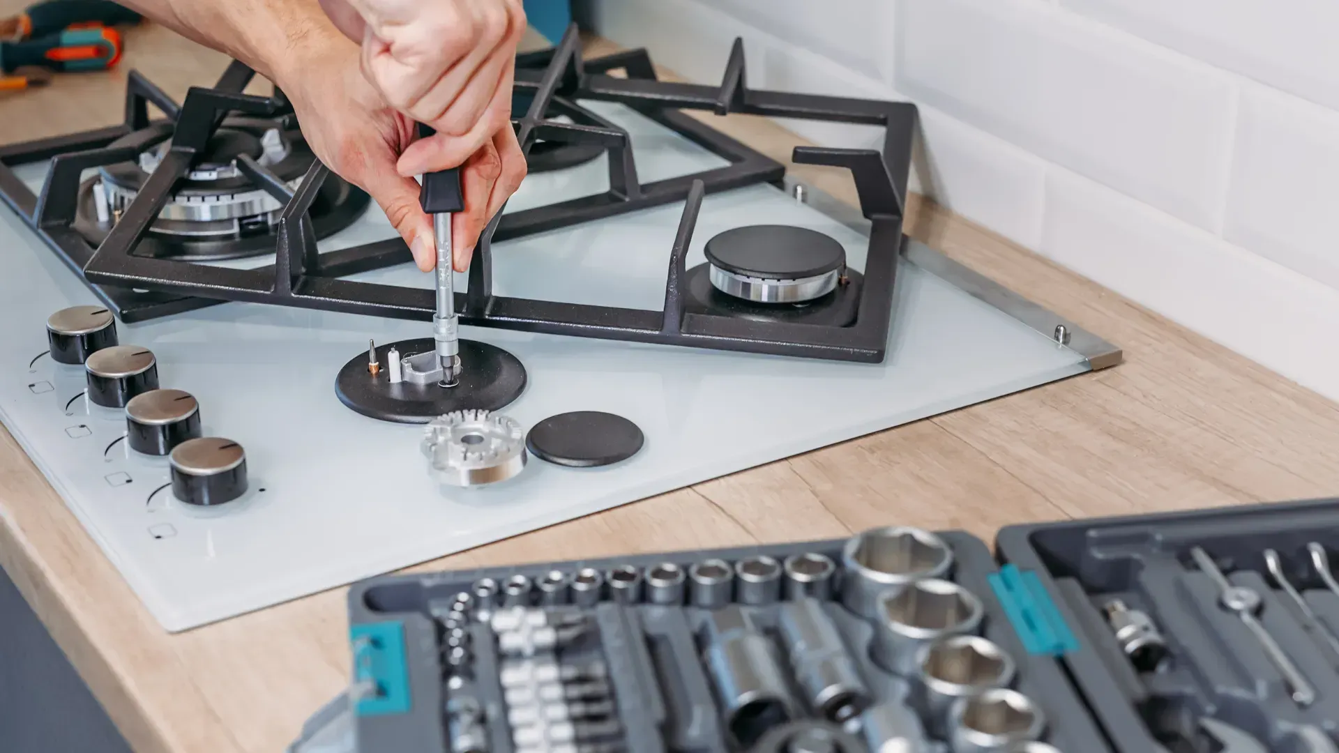 A man is fixing a gas stove with a screwdriver.