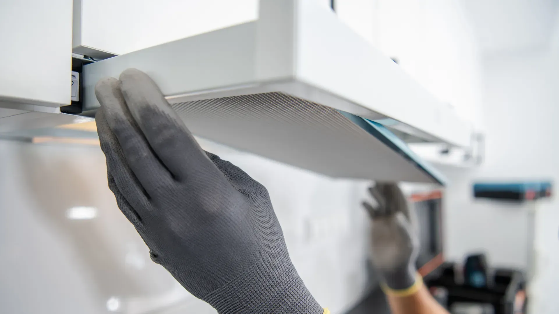 A person wearing gloves is cleaning a hood in a kitchen.