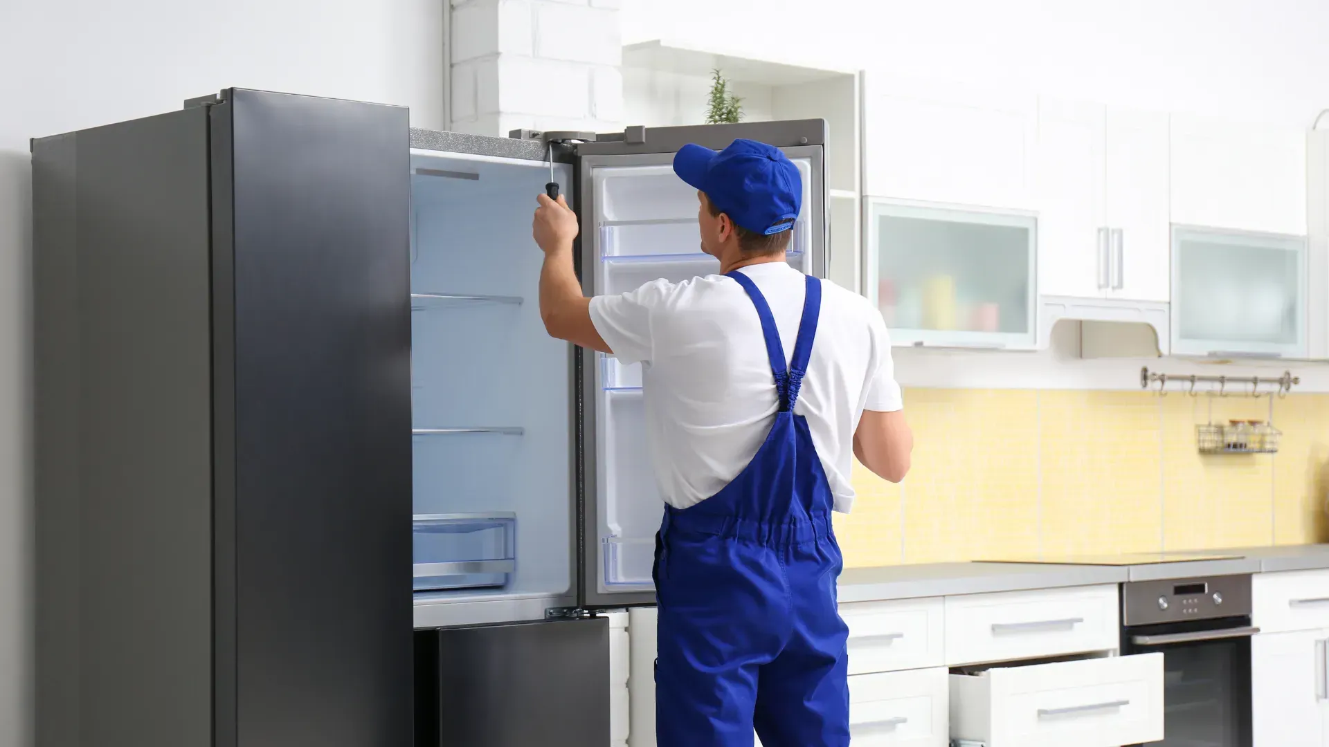 A man is fixing a refrigerator in a kitchen.