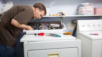 A man is fixing a washer and dryer in a laundry room.