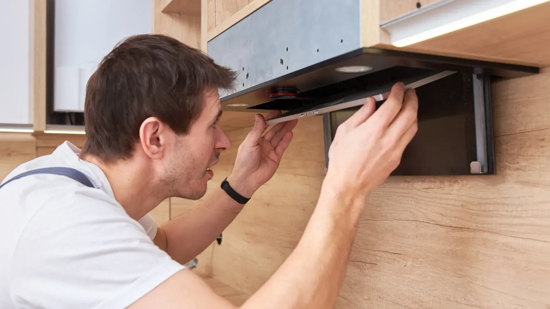 A man is fixing a kitchen hood with a screwdriver.