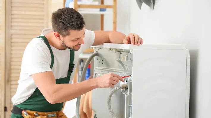 A man is fixing a washing machine in a laundry room.