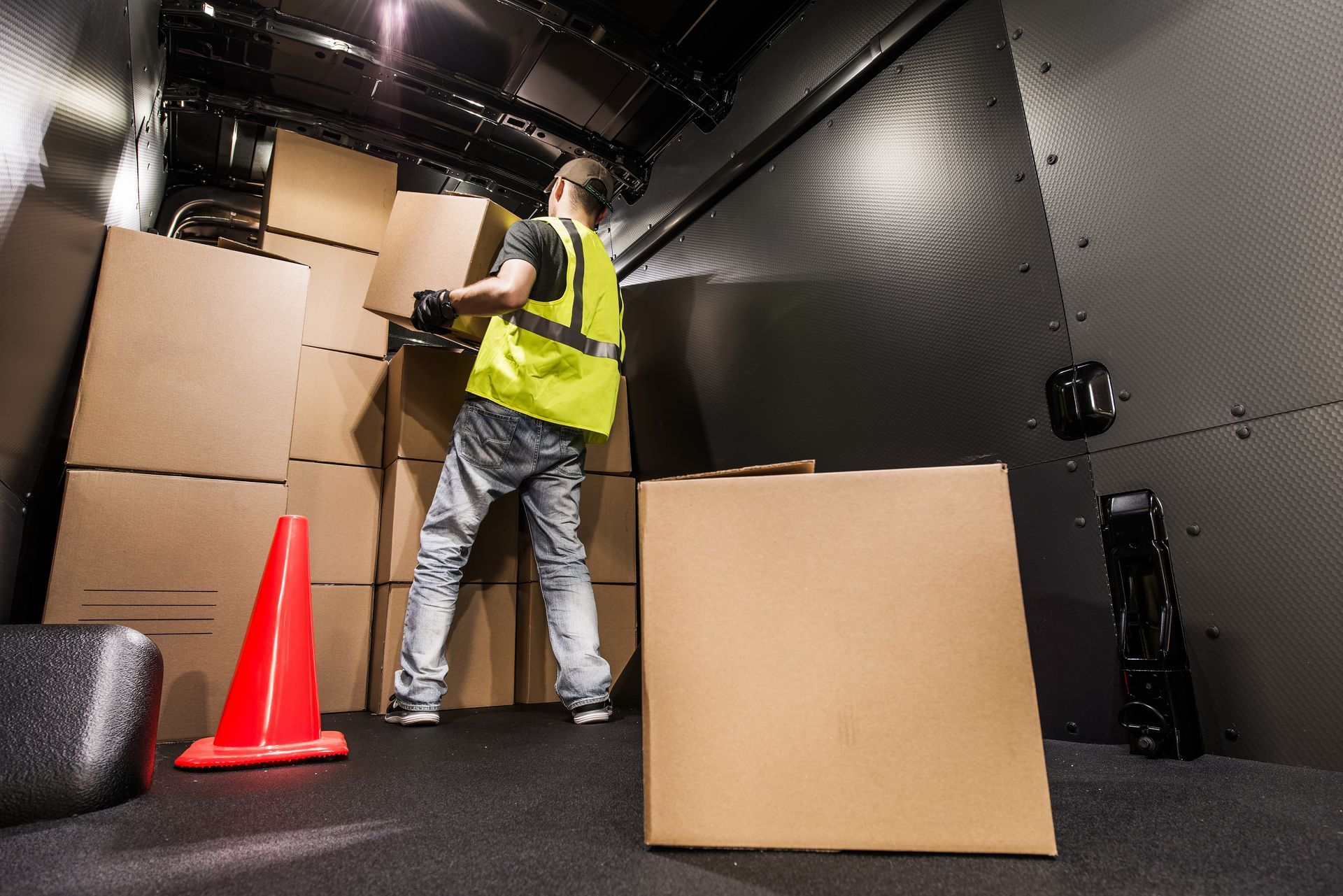 A man in a yellow vest is loading boxes into a truck.