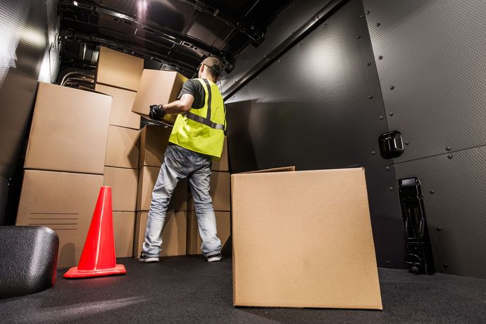 A man in a yellow vest is loading boxes into a truck.