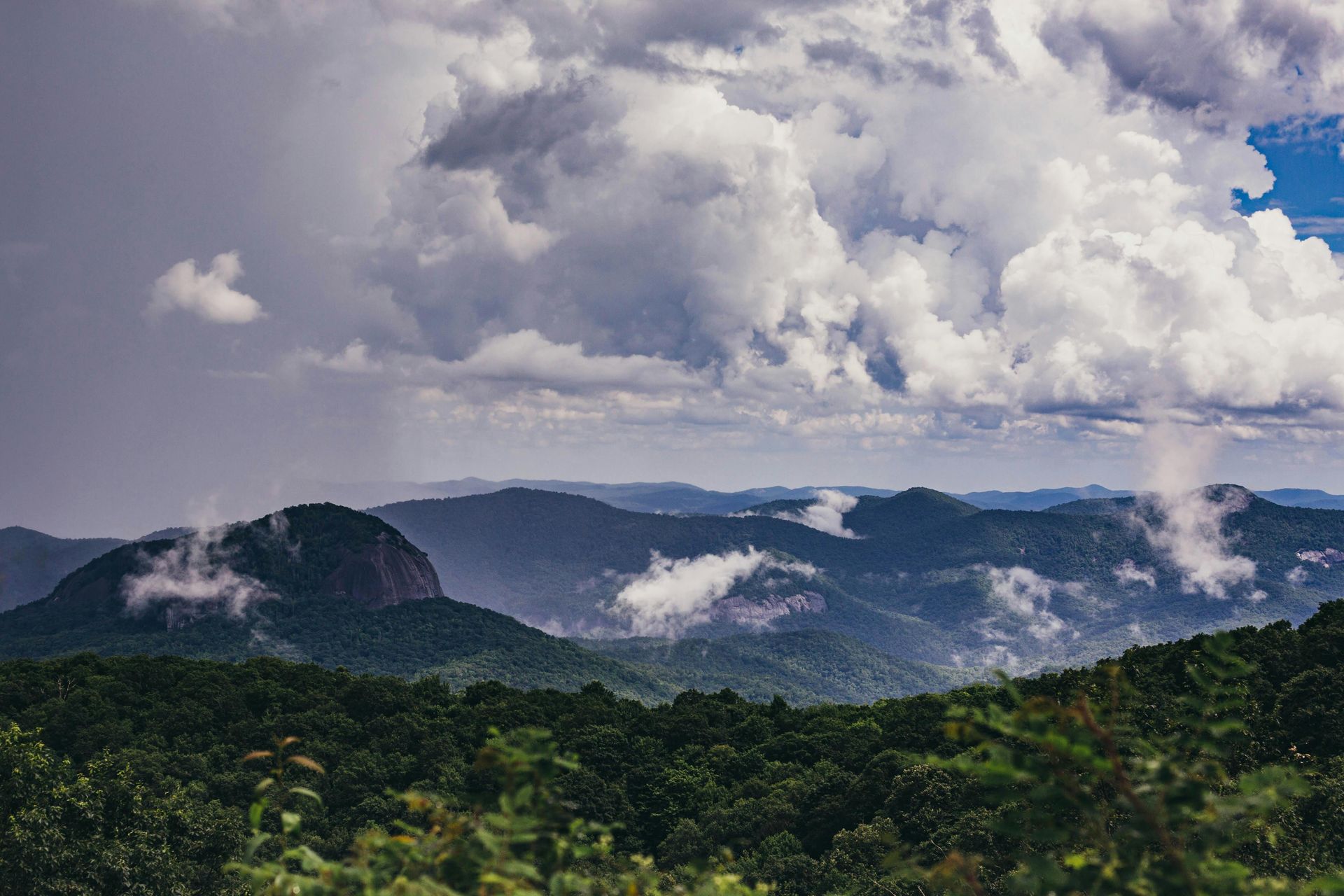 A view of a mountain range with trees and clouds in the sky.