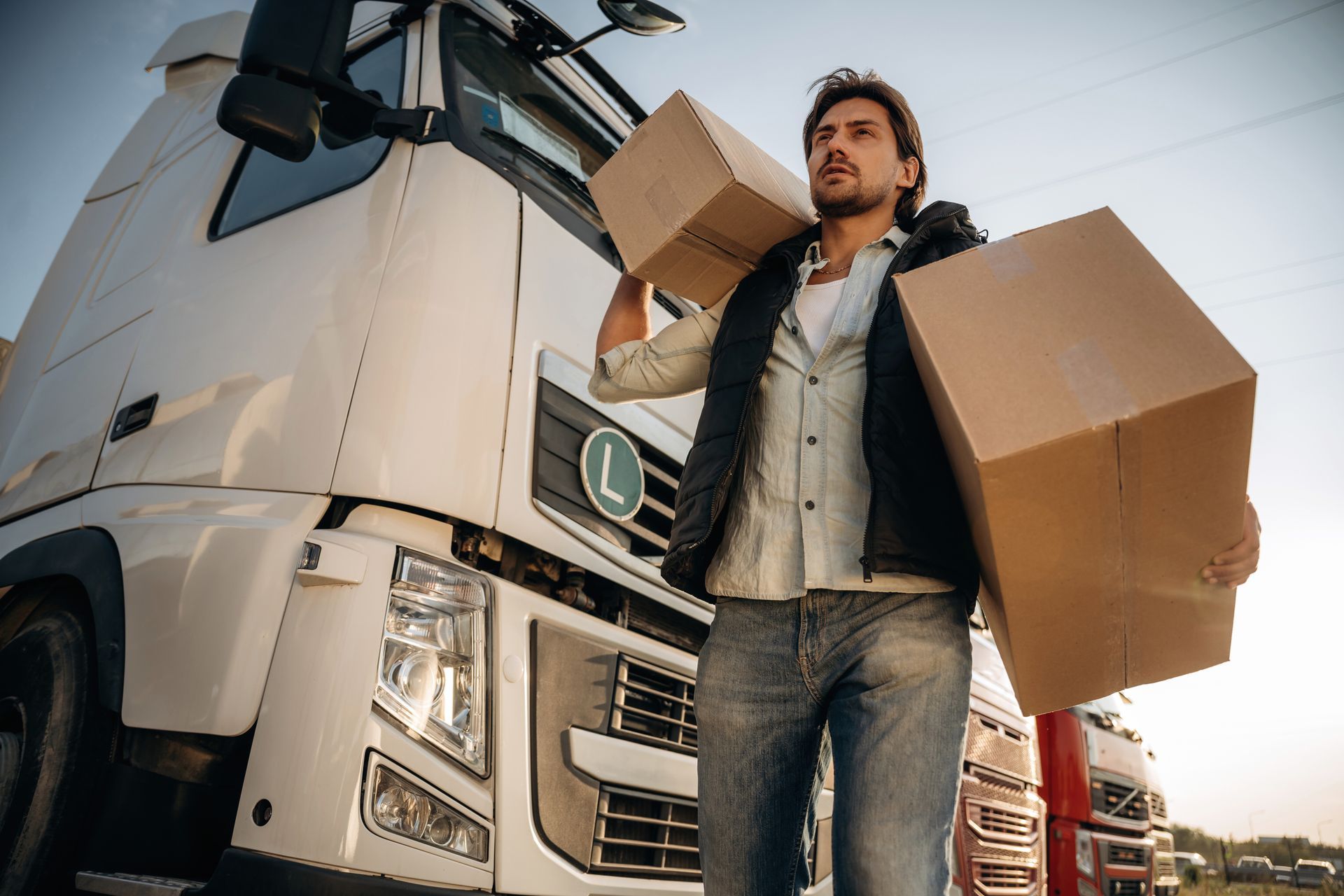 A man is carrying boxes on his shoulder in front of a truck.