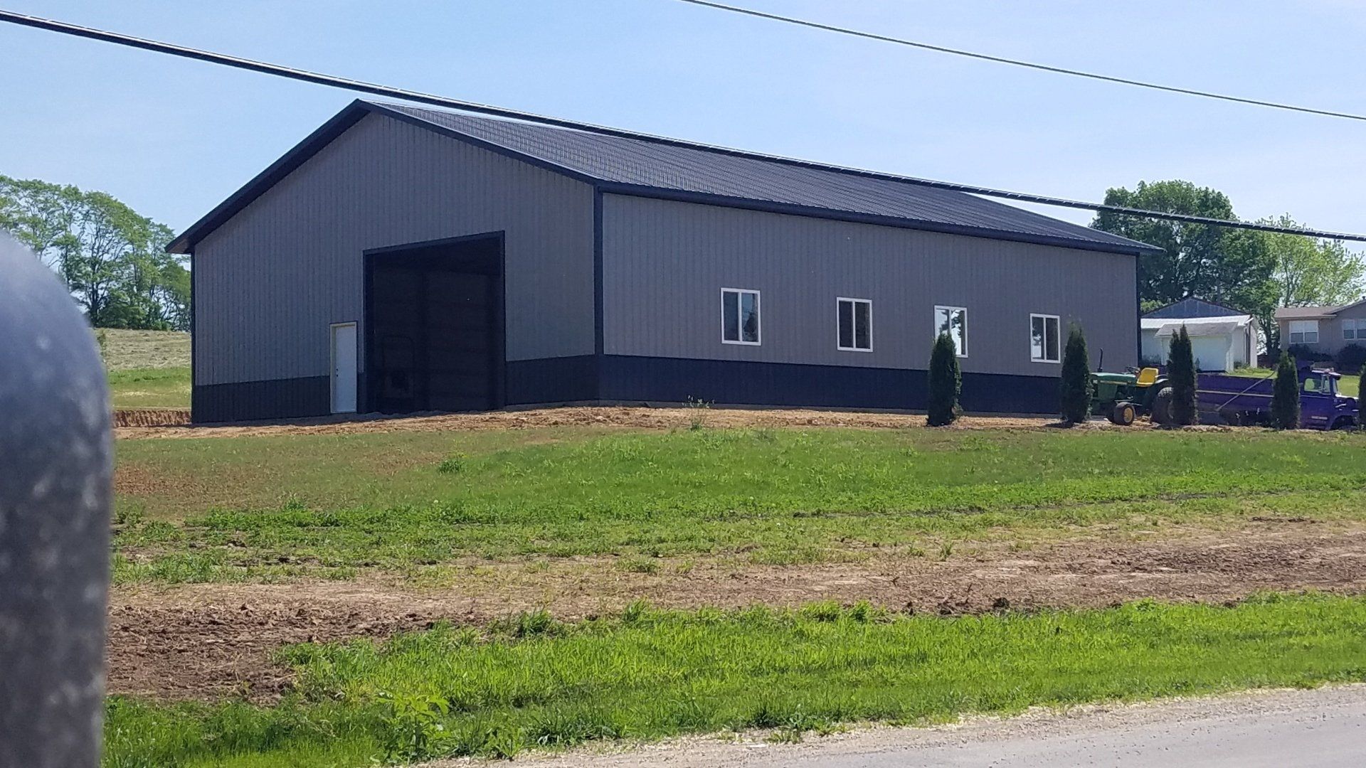 Gray metal barn with black accents, set in a field with green grass. Three windows.
