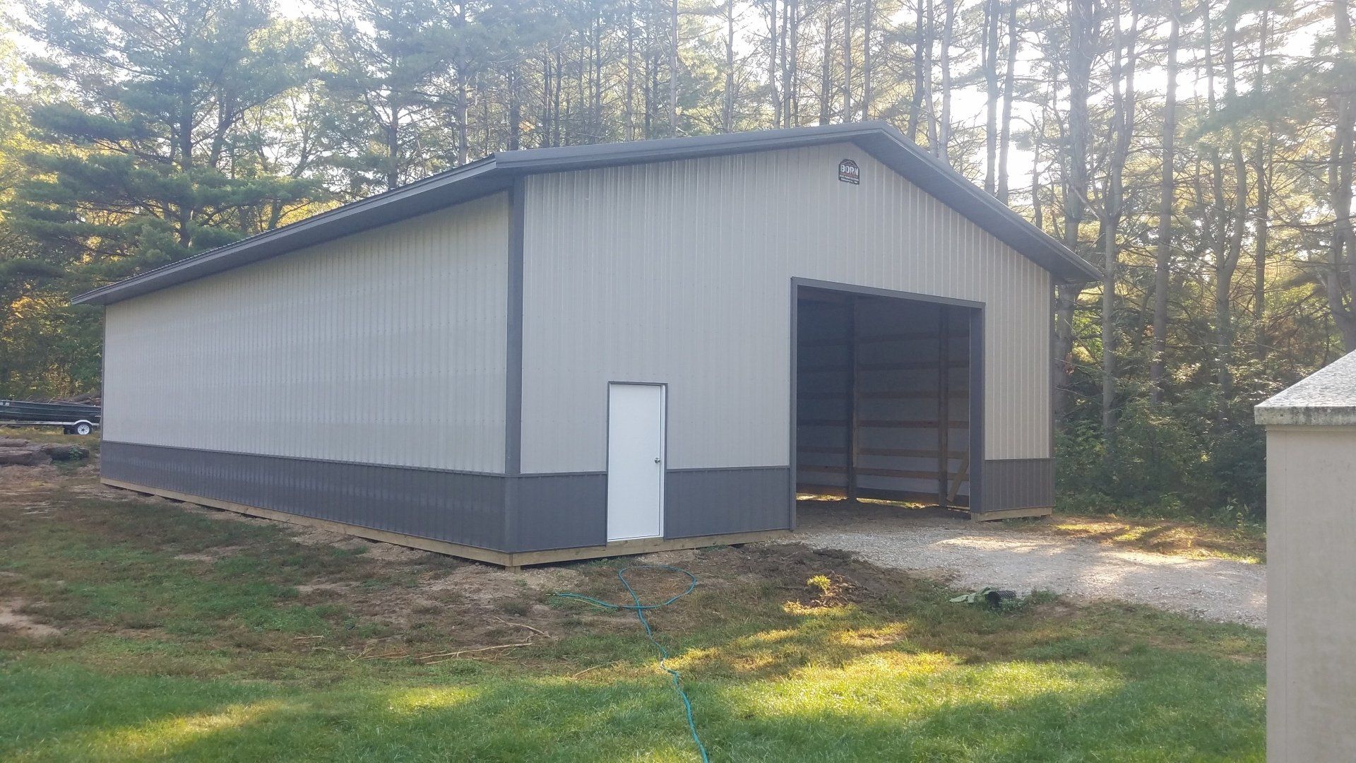 Gray metal barn with open door and small white door, surrounded by trees.