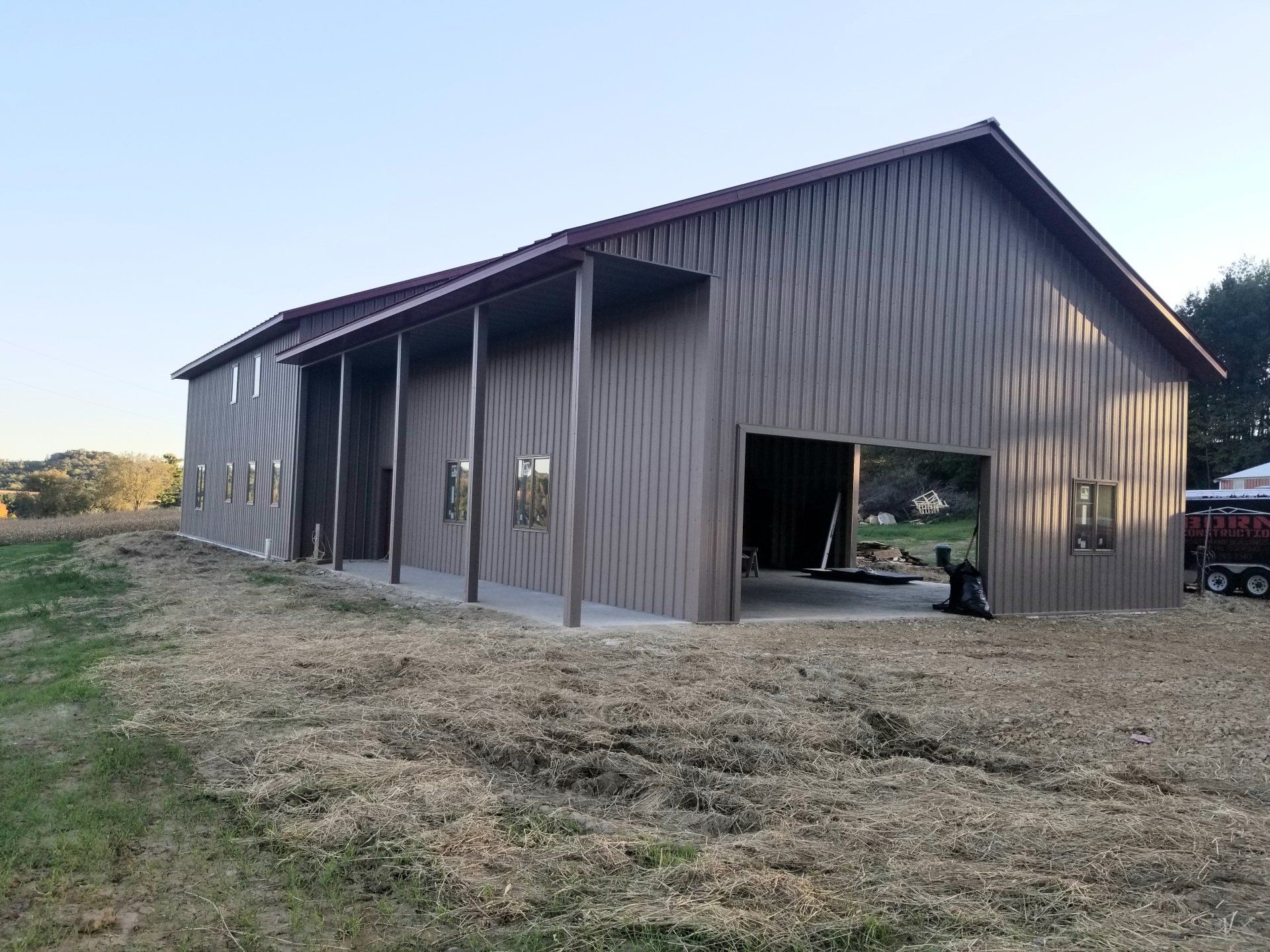 Brown metal barn with a covered porch and open doorway, set in a field.