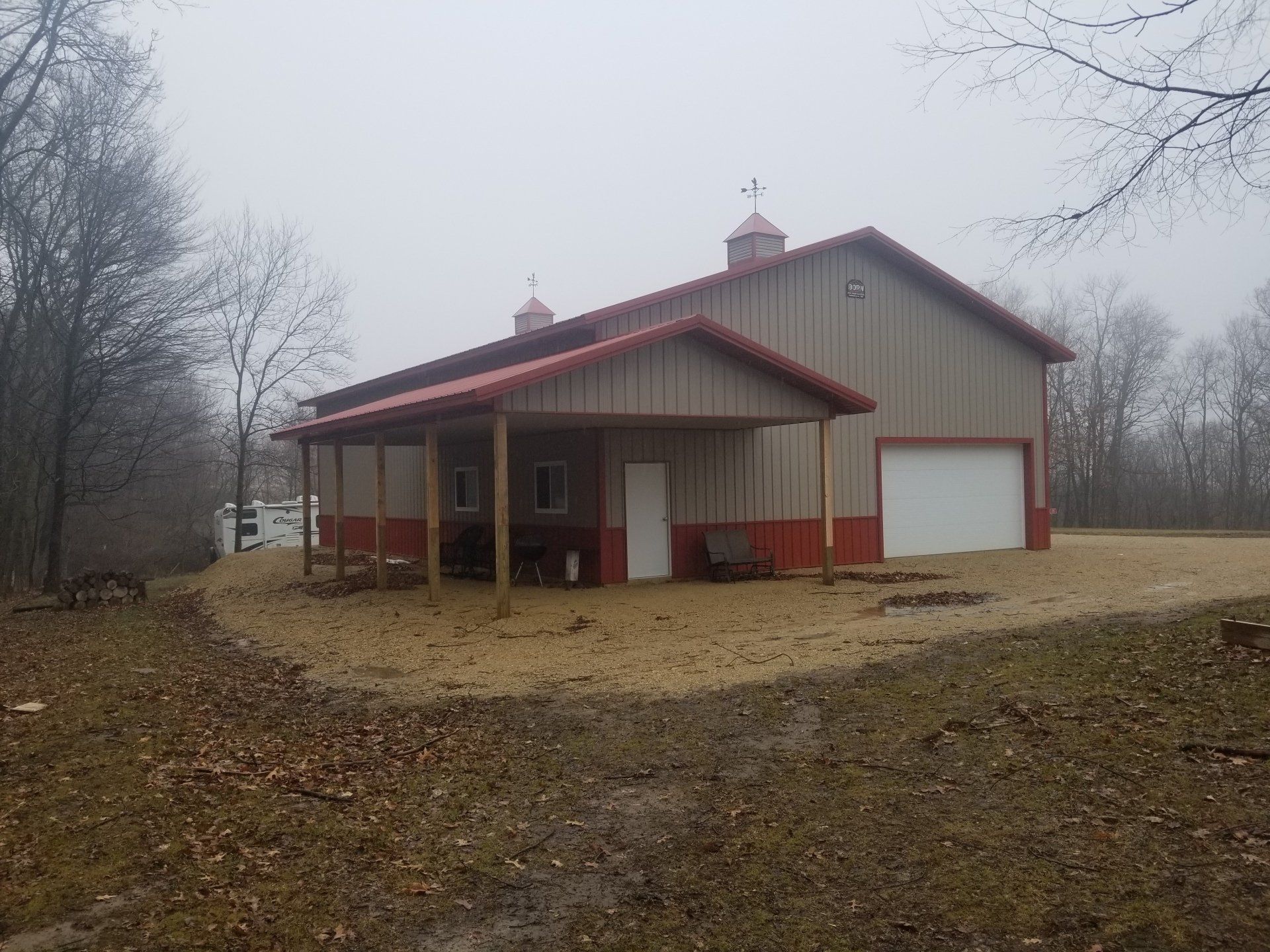 Tan and red barn with a covered porch on a cloudy day.