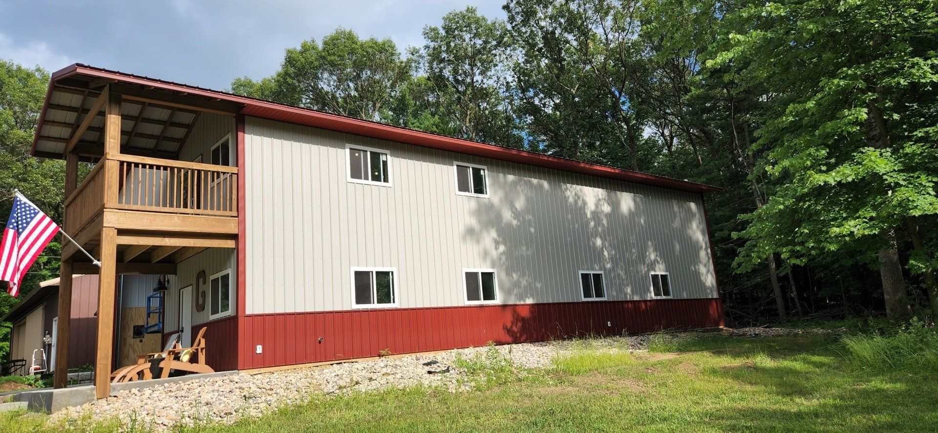 Two-story house with a wooden balcony and American flag. Red and white exterior. Set in a grassy yard.