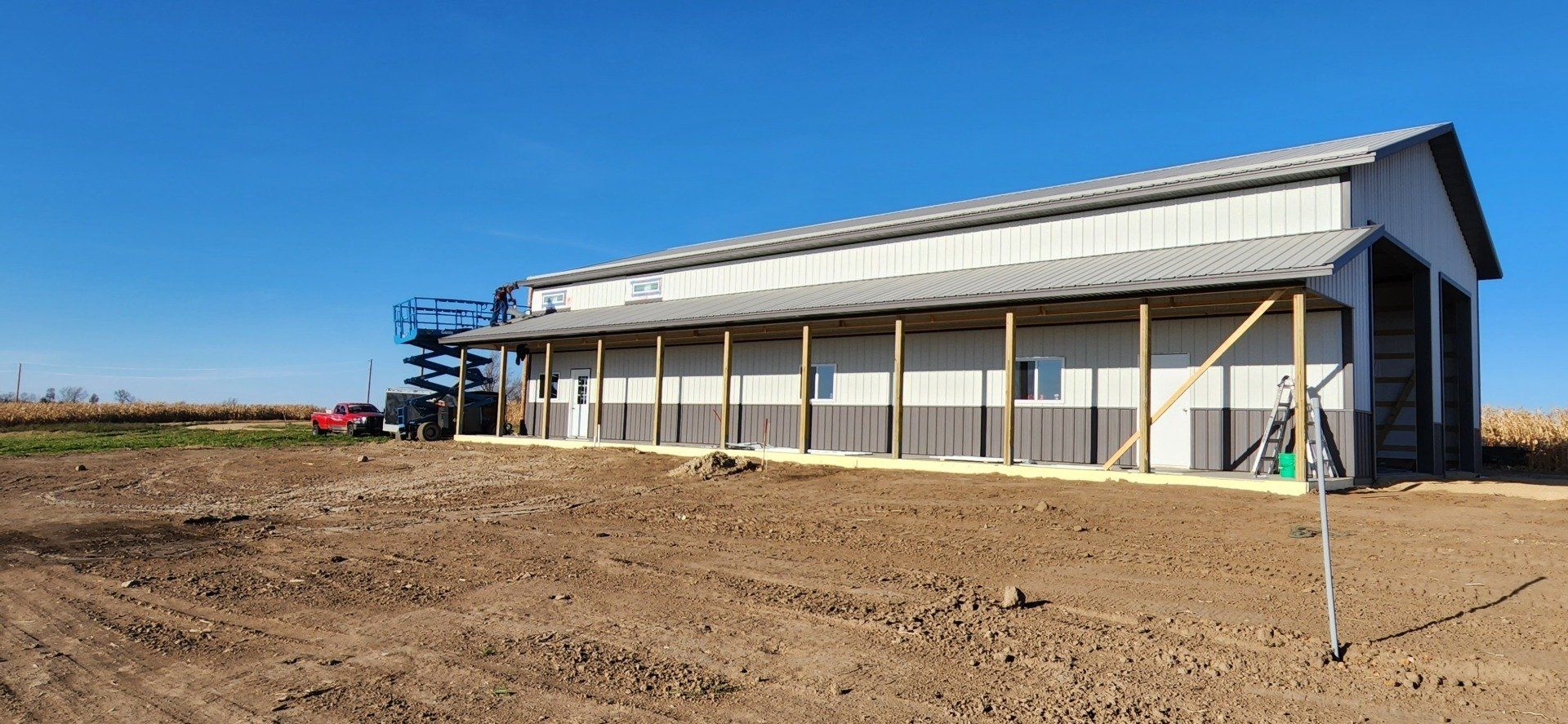 Large metal building with a covered porch on a dirt lot under a blue sky.