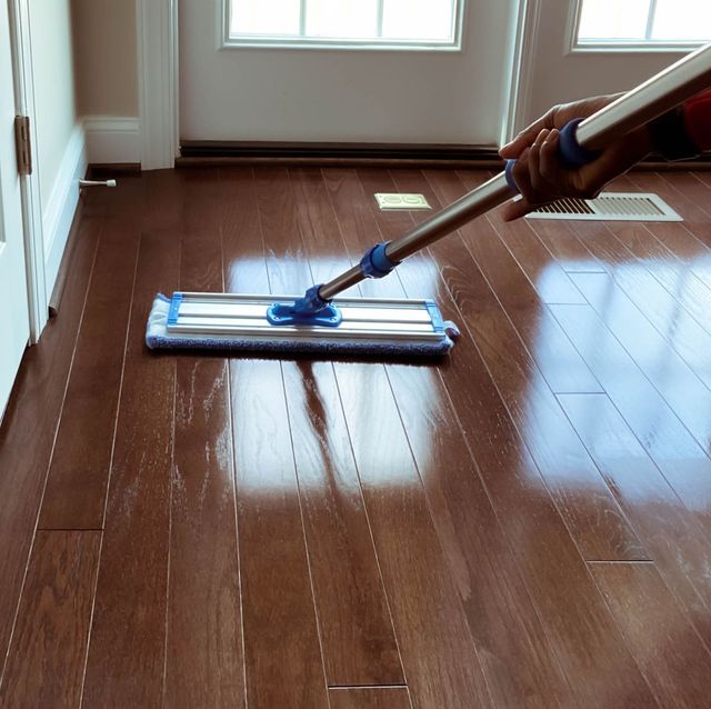 A person mopping a shiny hardwood floor near a window.