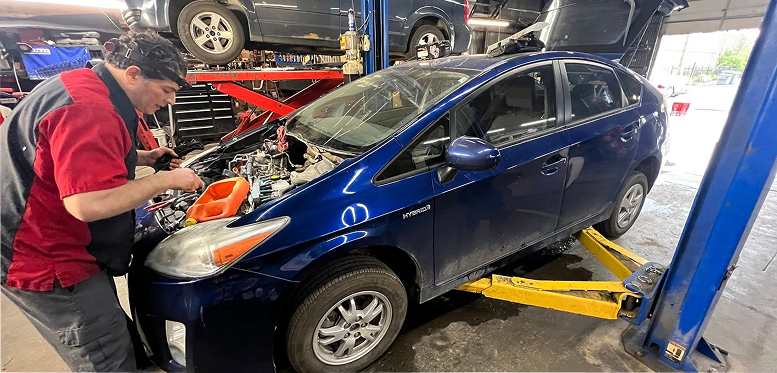 A man is working on the engine of a blue car on a lift.